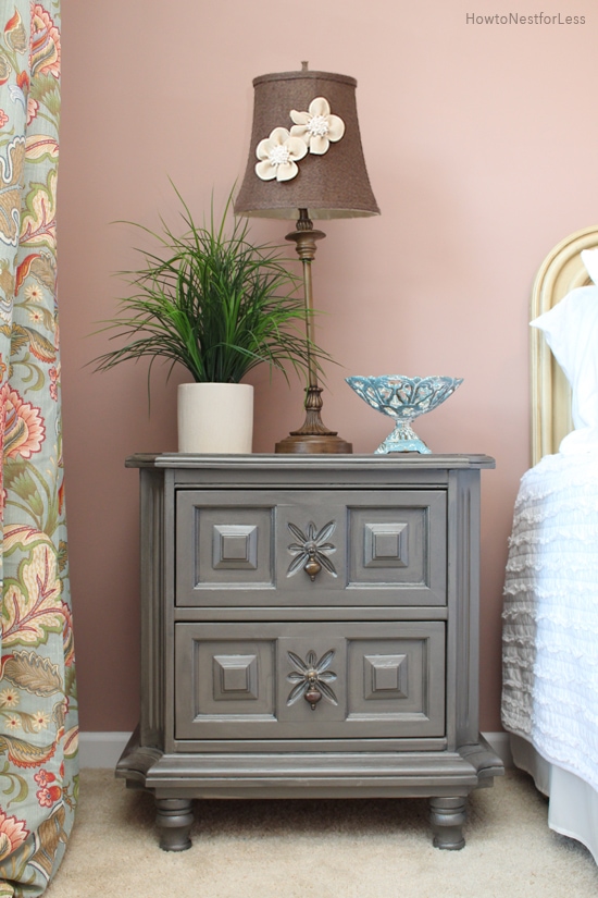 在床旁边的一个灰色床头柜与对此的一盏灯，碗和盆的植物。